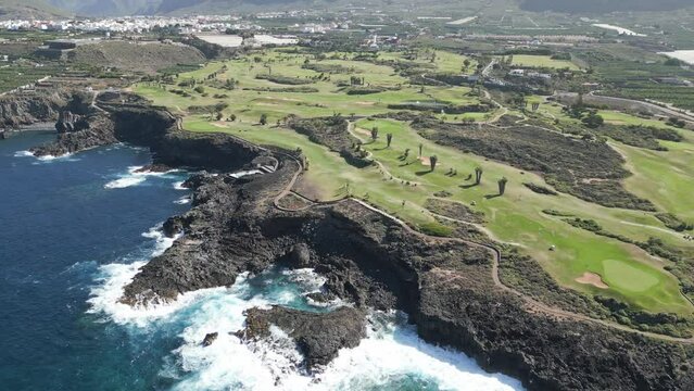 Epic cliffside golf course looks over beautiful blue ocean in Tenerife Spain, aerial parallax