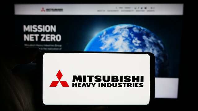 Stuttgart, Germany - 11-28-2023: Person holding smartphone with logo of Japanese company Mitsubishi Heavy Industries Ltd. (MHI) in front of website. Focus on phone display.