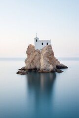 Minimal long exposure Photography of a white and blue church on a rock in the middle of the sea on a Greek island - obrazy, fototapety, plakaty