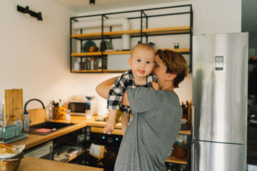 A mother holds her daughter in her arms in the kitchen. Normal mom routine. Lifestyle