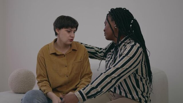 Loving caring beautiful black female talking to upset depressed young friend, caring girl giving support advise understanding empathy to stressed adult caucasian woman. Serious conversation