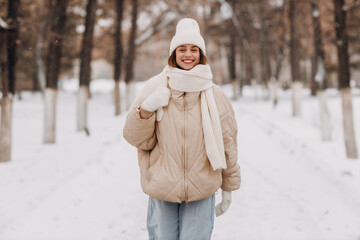 Happy smiling young woman dressed down jacket scarf hat and mittens enjoys winter weather and walking through the snowy winter park © primipil