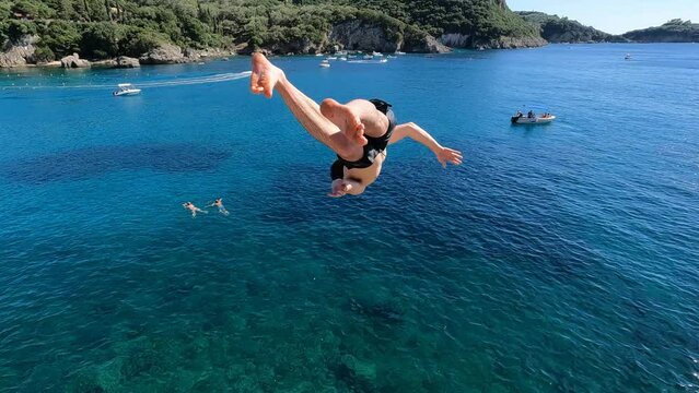 Adventurous young man jumping off a cliff does a backflip in Greece