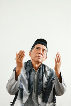 Senior elderly Asian muslim man in muslim clothes raising hands and praying isolated over white background