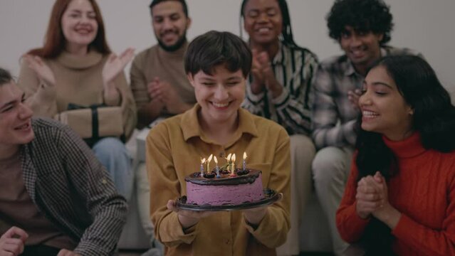 Happy multiracial friends congratulating with birthday excited pretty girl, celebrating fun party. Racial Friends resting together, laughing, blowing candles on cake, singing song, clapping 
