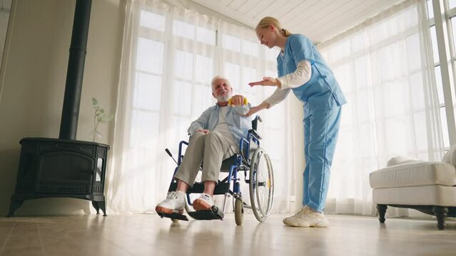 Man in wheelchair exercising with nurse. Social medical worker woman helping senior male doing physical hands exercises with dumbbell. Palliative care in late stage of neurodegenerative pathologies.