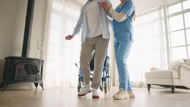Nurse helps old wheelchair man to walk. Physical therapist woman provides medical help support to senior male training studying to go. Recuperation after trauma, injury, temporary paralysis concept.