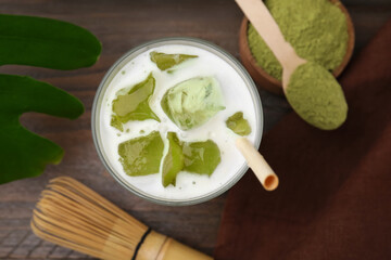 Glass of tasty iced matcha latte, bamboo whisk and powder on wooden table, flat lay