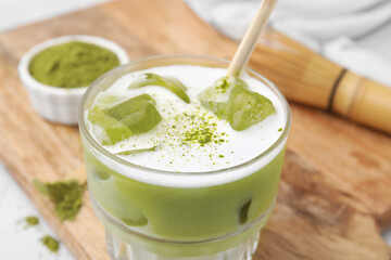 Glass of tasty iced matcha latte on wooden board, closeup