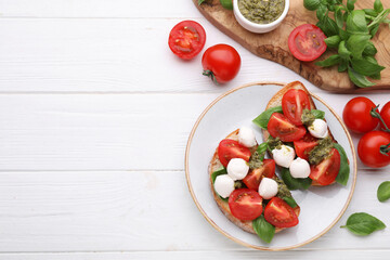 Delicious Caprese sandwiches with mozzarella, tomatoes, basil and pesto sauce on white wooden table, flat lay. Space for text