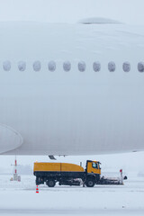 Winter frosty day at airport during heavy snowfall. Airplane covered with snow against snowplows...