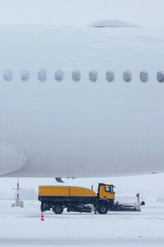 Winter frosty day at airport during heavy snowfall. Airplane covered with snow against snowplows clearing airport runway..