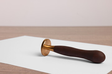 One stamp tool and sheet of paper on wooden table, closeup