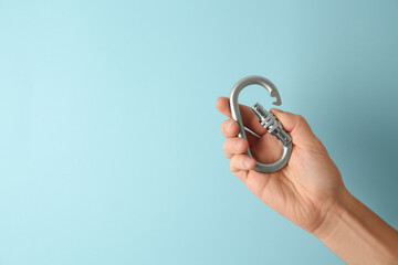 Man with metal carabiner on light blue background, closeup. Space for text