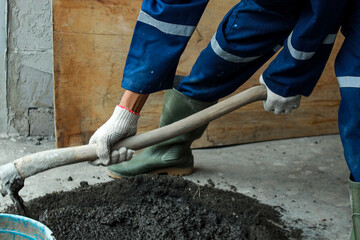 Male worker with safety rubber boot and uniform using hoe to mixing sand, cement and water for home...