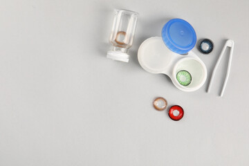 Different color contact lenses, tweezers and containers on light background, flat lay. Space for text