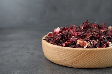 Hibiscus tea. Wooden bowl with dried roselle calyces on grey table, closeup. Space for text