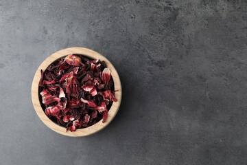 Hibiscus tea. Wooden bowl with dried roselle calyces on grey table, top view. Space for text