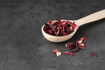 Hibiscus tea. Wooden spoon with dried roselle calyces on grey table. Space for text