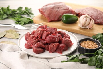 Plate with pieces of raw beef meat, spices and products on table