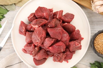 Plate with pieces of raw beef meat on light wooden table, top view