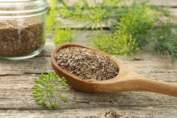 Spoon with dry seeds and fresh dill on wooden table, closeup