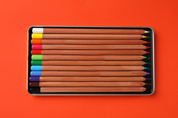Box with many colorful pastel pencils on orange background, top view. Drawing supplies