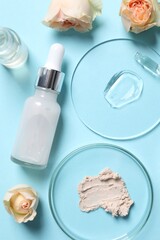 Fototapeta na wymiar Bottle of cosmetic serum, flowers and petri dishes with samples on light blue background, flat lay
