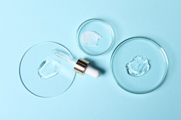 Pipette, cosmetic serum and petri dishes with samples on light blue background, flat lay