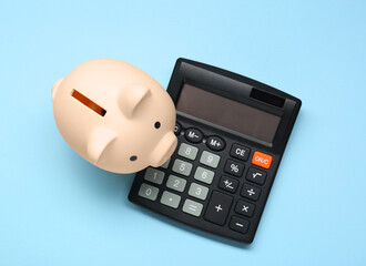 Calculator and piggy bank on light blue background, top view