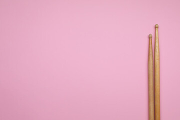 Two wooden drum sticks on pink background, top view. Space for text