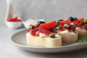 Delicious sandwiches with bresaola, cream cheese, olives and tomato on light grey table, closeup