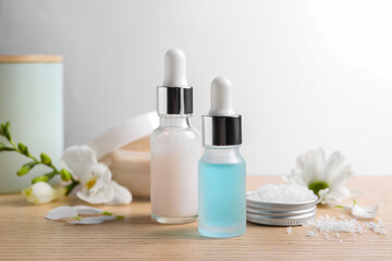 Fototapeta na wymiar Bottles of cosmetic serum, sea salt and beautiful flowers on wooden table, closeup