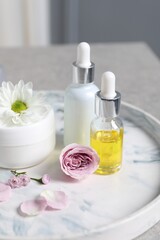 Fototapeta na wymiar Bottles of cosmetic serum, cream jar and flowers on table, closeup