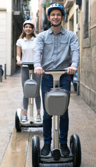 Fototapeta na wymiar Young couple guy and girl walking on segway in streets of european city