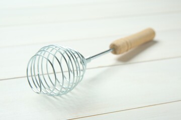 Metal spring whisk on white wooden table, closeup