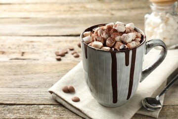 Delicious hot chocolate with marshmallows and cocoa powder in cup on wooden table, space for text