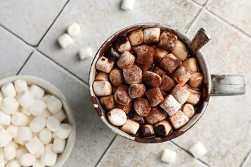 Delicious hot chocolate with marshmallows, cocoa powder and spoon in cup on tiled table, top view