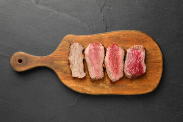 Delicious sliced beef tenderloin with different degrees of doneness on black table, top view
