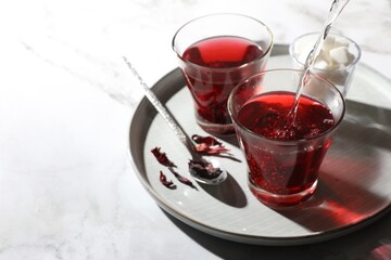 Making hibiscus tea. Pouring hot water into cup with roselle petals at white table. Space for text
