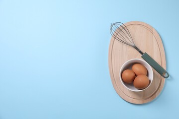 Metal whisk and raw eggs on light blue background, top view. Space for text