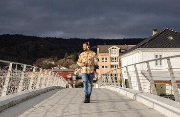 Attractive smiling adult man walking through a city in Norway while listening to music on his phone with his headphones