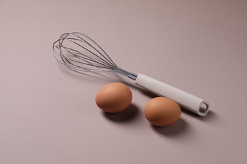 Metal whisk and raw eggs on grey background