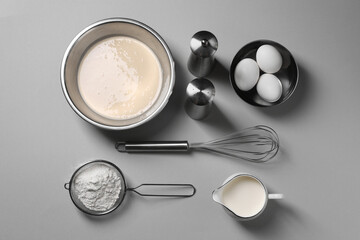 Flat lay composition with dough in bowl and metal whisk on grey background