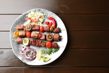 Delicious shish kebabs with vegetables on wooden table, top view. Space for text