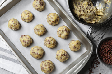 Baking pan with raw chocolate chip cookie balls, ingredients and whisk on table, flat lay