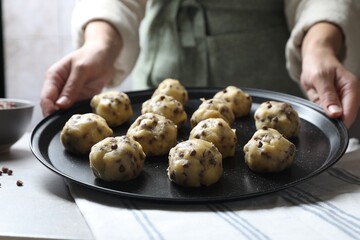 Woman putting tray with raw chocolate chip cookie balls on table indoors, closeup