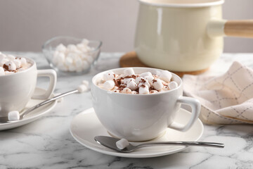 Aromatic hot chocolate with marshmallows and cocoa powder served on white marble table, closeup