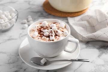 Cup of aromatic hot chocolate with marshmallows and cocoa powder served on white marble table, closeup