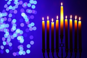 Hanukkah celebration. Menorah with burning candles on blue background with blurred lights, space for text